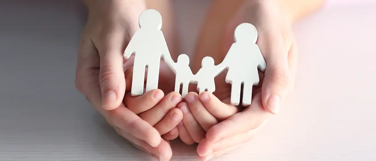 concept image of adult and child's hands holding a paper cut out of a family.